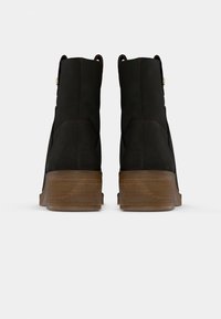 Bottes noires à la cheville en matériau lisse et à bout rond. Dotées d'un talon en bois empilé et de petits accents dorés.