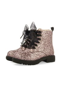 Botines brillantes de color rosa con parte delantera negra con cordones, acentos de cinta transparente, suelas gruesas y un acabado metálico en el tacón.
