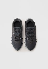 Baskets de sport grises avec une tige texturée, des lacets et un rembourrage en air visible dans la semelle. Présente un design élégant et arrondi avec des accents de logo.