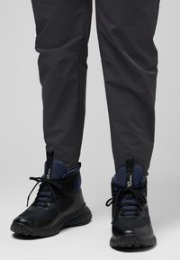Schwarze und marineblaue Wanderschuhe mit strukturierten Gummisohlen, gepolsterten Kragen und Schnürungen, kombiniert mit dunkelgrauen Hosen.