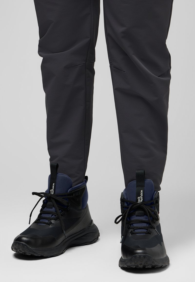 Schwarze und marineblaue Wanderschuhe mit strukturierten Gummisohlen, gepolsterten Kragen und Schnürungen, kombiniert mit dunkelgrauen Hosen.