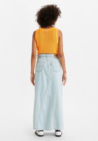 Top giallo lavorato a maglia senza maniche con motivo strutturato, abbinato a una lunga gonna in denim blu chiaro con doppie tasche posteriori e sneakers bianche.