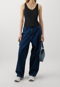 Top in cotone nero a coste, pantaloni in denim blu a gamba larga, sneakers bianche e una piccola borsa grigia. Design semplice con una vestibilità comoda.