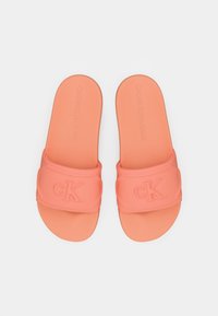 Oransje sklisikre sandaler med teksturert stropp og preget "ck"-logo. Glatt såle og avrundet, åpen tådesign.