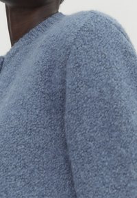 Pull en maille texturée bleu clair avec un col rond et des bordures côtelées, fabriqué dans un matériau doux et duveteux, et avec une coupe décontractée.