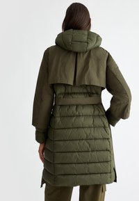 Olijfgroene pufferjas met een afneembare capuchon, een riem in de taille en gequilte textuur, met een cape-achtige achterkant en lange mouwen.