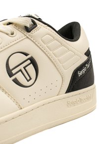 Beige bőr sneaker fekete akcentusokkal. Kerek logóval, perforációkkal és texturált talppal rendelkezik. Kötelek és párnázás látható.