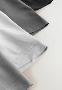 Tres camisetas en diferentes tonalidades de gris, con mangas cortas y fabricadas en suave algodón. Costuras visibles en cada dobladillo.