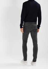 Grå jeans i denim med smal passform, kontrasterande sömmar och två bakfickor. Kombinerade med en figurnära svart tröja och vita sneakers.