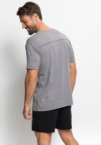 Graues T-Shirt mit kurzen Ärmeln und Rundhalsausschnitt, glatte Textur und kontrastierende Nähte auf dem Rücken, kombiniert mit schwarzen Shorts.