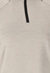 Lichtgrijze rits-top met textuurstof, voorzien van een zwarte rits en kraagaccenten, ontworpen voor comfort en veelzijdigheid.