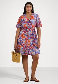 Cvečna obleka iz lahkega blaga, ki vključuje odtenke modre, oranžne in rožnate barve. Ima kratke fltrajoče rokave in pas z vezavo. Dodatki vključujejo majhno tkanino torbico.