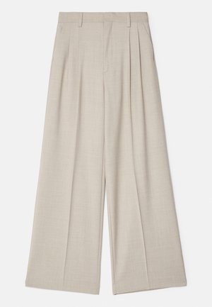 Pantalons larges beiges avec une texture lisse, dotés de plis à l'avant, d'une taille plate et d'un design ajusté pour une coupe décontractée.