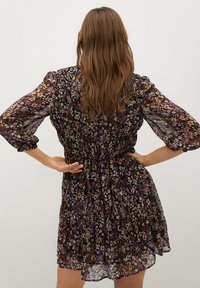 Robe florale courte avec une taille froncée, fabriquée en tissu léger. Elle possède des manches bouffantes et un fond sombre avec des motifs de fleurs colorées.