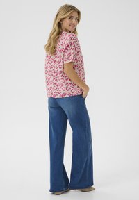 Top rosa a maniche corte con stampa leopardata abbinato a jeans blu a gamba larga. Il tessuto sembra morbido e i jeans hanno una classica trama denim.