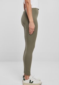 Olijfgroene legging gemaakt van een rekbare katoenmix, met een slim fit en enkellange ontwerp, gecombineerd met witte sneakers.