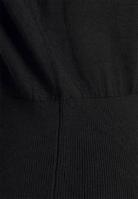Gros plan d'un tissu noir tricoté montrant des coutures côtelées et texturées détaillées avec des zones froncées et lisses.