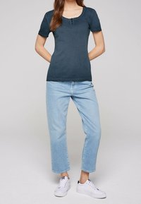 Námořnické tričko s krátkým rukávem a kulatým výstřihem, ozdobené třemi knoflíky, v kombinaci se světle modrými rovnými džíny a bílými teniskami.