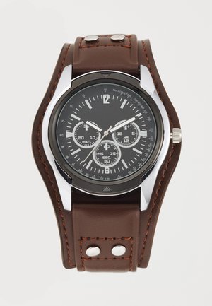 Brown leather watch with silver accents, black dial, three sub-dials, tachymeter markings, and stitched strap featuring two metal studs.