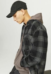 Zwart en grijs geruite flanellen shirt met een grijze hoodie eronder, gecombineerd met een zwarte pet, vanaf de zijkant weergegeven.