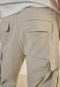 Pantalones cargo de color beige claro con dos bolsillos traseros y parches de refuerzo en las rodillas. La tela tiene una textura suave y duradera y un diseño de pierna recta.
