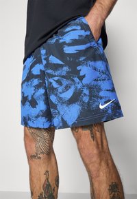 Shorts blu e neri con design astratto a pennellate. Presenta il logo Nike in bianco. Realizzati in materiale leggero.