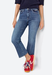 Jean court bleu foncé avec une taille ajustée et une légère évasement aux chevilles. Associé à des baskets rouges avec des lacets multicolores.