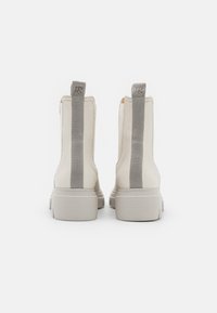 Botas de tobillo de cuero blanco con paneles laterales elásticos grises y tiradores, que cuentan con suelas de goma texturizada y un diseño de punta redonda.