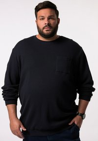 Tummansininen pitkähihainen crewneck-sweatshirt, jossa on teksturoitu kangas, etupocket ja rento istuvuus. Yhdistetty sinisiin farkkuihin ja kelloon.