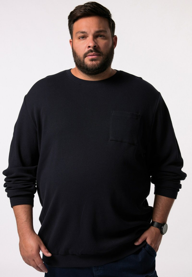 Tummansininen pitkähihainen crewneck-sweatshirt, jossa on teksturoitu kangas, etupocket ja rento istuvuus. Yhdistetty sinisiin farkkuihin ja kelloon.