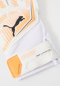 Weiße Handschuhe mit orangefarbenen Akzenten, strukturiertem Griffmuster, ausgestattet mit einem schwarzen Puma-Logo und einem Etikett, das "2MM SUPERSOFT" liest.