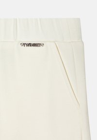 Kreemjoggerid pehme tekstuuriga, laia elastse vöökoha ja väikese hõbedase "TWINSET" logoga ees. Kaks küljetaskut.