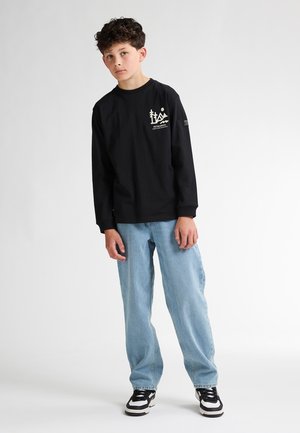 Schwarzes langärmliges Shirt mit weißem Grafikdesign auf der Vorderseite. Kombiniert mit hellblauen weiten Jeans und schwarzen Sneakers.