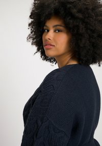 Maglione lavorato a maglia blu scuro con motivi a treccia sulle maniche e colletto a coste, caratterizzato da una vestibilità rilassata e un tessuto morbido.