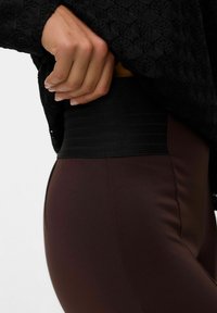 Hoge taille legging in donkerbruin met een gladde textuur. De tailleband heeft subtiele ribbels in zwart voor extra ondersteuning.