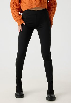 Leggings negras con textura suave, cintura alta y diseño ajustado, combinadas con un suéter corto de punto naranja con textura.