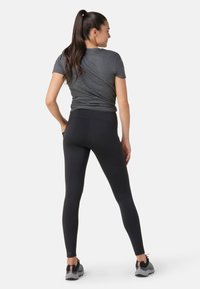 Svarta leggings med hög midja, tillverkade av smidigt, stretchigt tyg. Kombinerat med en åtsittande grå t-shirt och sportskor.