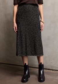 Jupe midi à imprimé léopard en tissu gris foncé, présentant une texture douce et une silhouette droite, associée à des bottines noires.