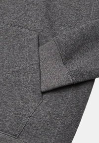 Grå sweatshirt med et blødt, tekstureret stof, skrå lomme, ribbede manchetter og syninger, der viser et enkelt og funktionelt design.