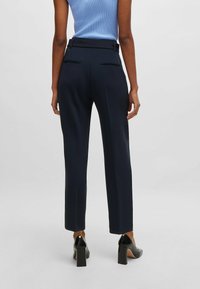 Pantaloni tailleur blu navy con una texture liscia, vestibilità slim e doppie tasche posteriori. Abbinati a scarpe nere con tacco alto.