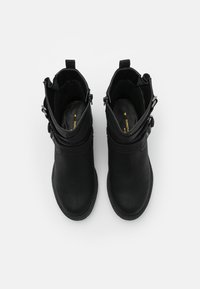 Botines negros con textura de cuero suave, detalles ajustables con hebillas, punta redonda y tacón corto, vistos desde arriba.