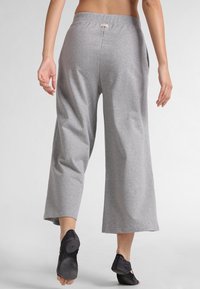 Szare bawełniane spodnie z szerokimi nogawkami i elastycznym pasem, wyposażone w boczne kieszenie i gładką fakturę. Noszone z czarnym obuwiem.