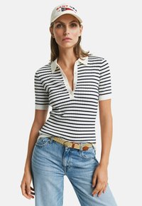 Randig stickad pikétröja i vitt och marinblått, med en mjuk halsringning, korta ärmar och ett strukturerat mönster. Tillsammans med ljusblå jeans och ett flätat bälte.