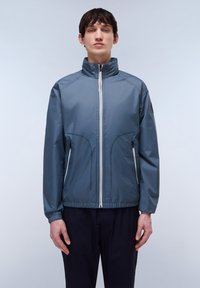 Lichte, blauwe windjack met een hoge kraag, voorritssluiting en elastische mouwen. Voert twee zijzakken met zwarte accenten.