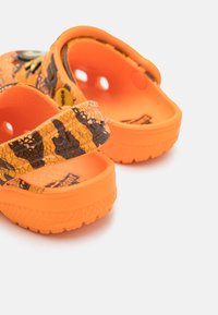 Lys orange klipklapper med et sort og gult slangemønster, der har to brede remme og ventilationshuller. Tekstureret sål for godt greb.