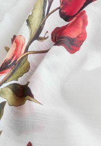 Auduma ar ziedu rakstu, kas attēlo sarkanas un rozā rozes ar zaļām lapām uz balta fona; viegls, caurspīdīgs tekstūra.