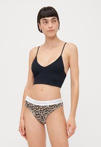 Čierny rebrovaný bralet s tenkými ramienkami, skombinovaný s nohavičkami s leopardím vzorom, ktoré majú biely pás so značkovaním.