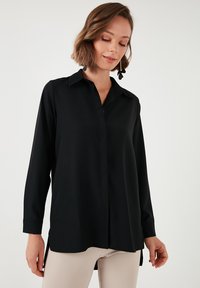 Black long-sleeve shirt with a pointed collar, button closure, and a straight cut. Features side slits, made of smooth fabric.