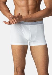 Boxers en coton blancs avec un waistband élastique gris comportant du texte imprimé. Le design inclut une coupe ajustée et une texture lisse.
