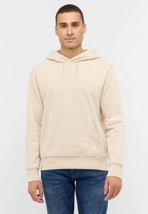 Beiger Hoodie aus weichem Stoff mit Kängurutasche, Kordelzug und gerippten Bündchen, kombiniert mit blauen Jeans. Einfaches und funktionales Design.